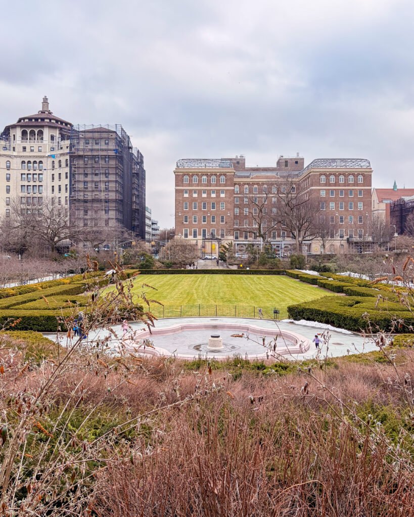 Uno scorcio suggestivo di un giardino ben curato all'interno di Central Park, New York, con palazzi stile liberty sullo sfondo