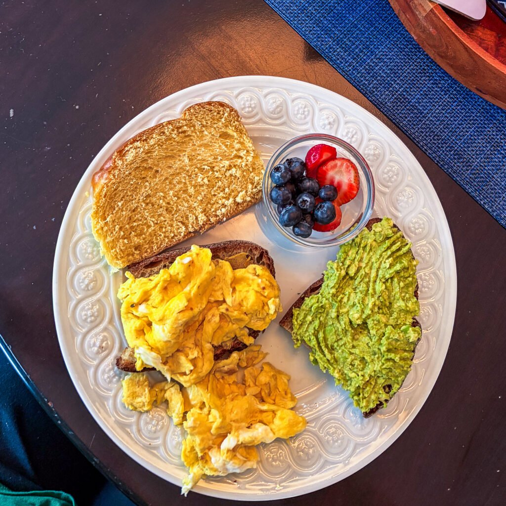 Una colorata colazione americana completa con avocado toast su pane rustico, uova strapazzate e una ciotola di frutta fresca mista
